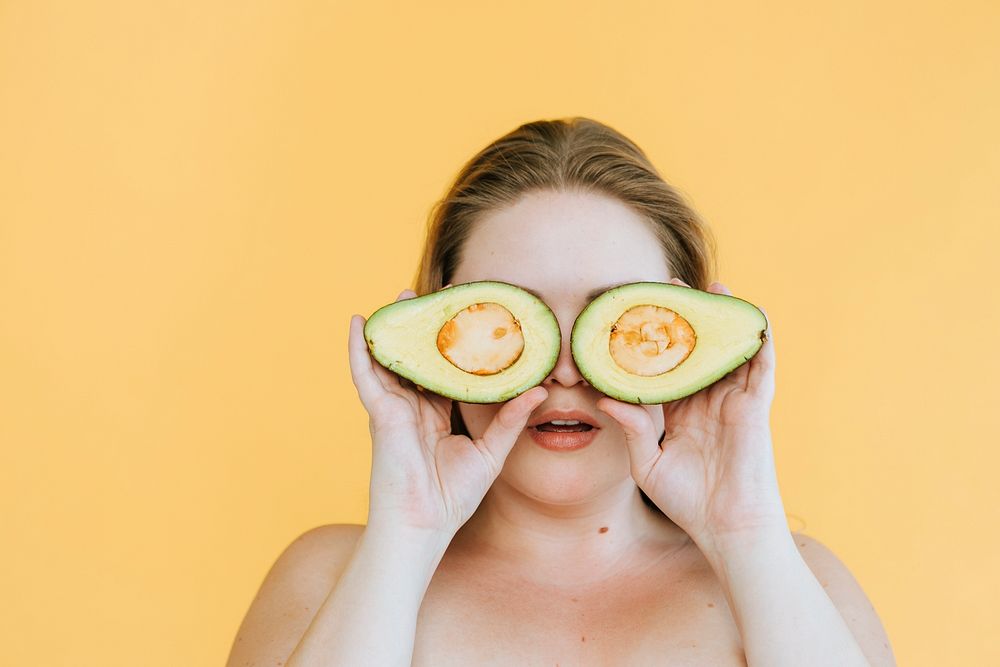 Happy woman holding freshly cut avocados over her eyes