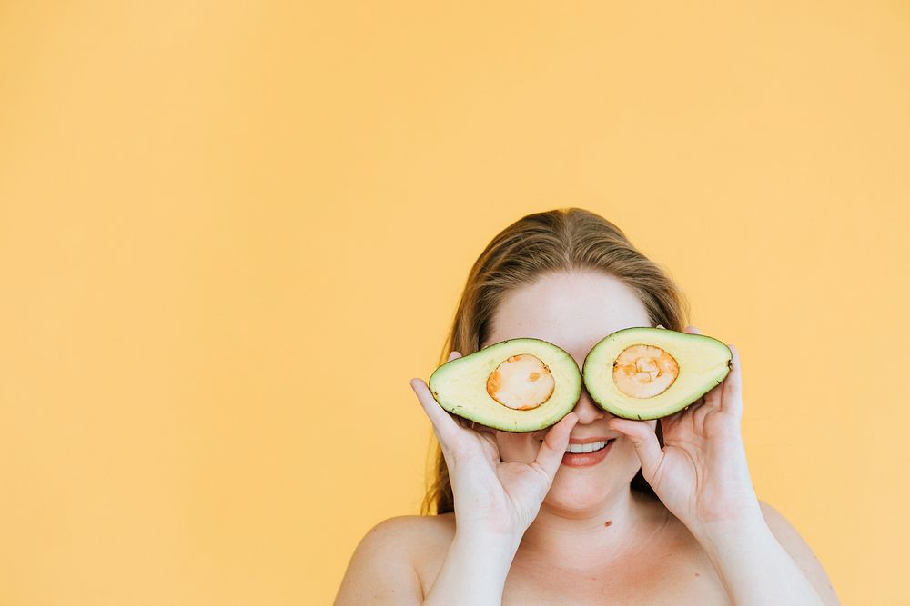 Happy woman holding freshly cut avocados over her eyes
