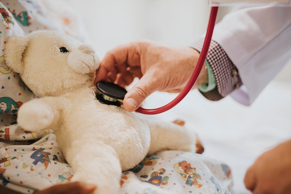 Doctor playfully checking the heart beat of a teddy bear