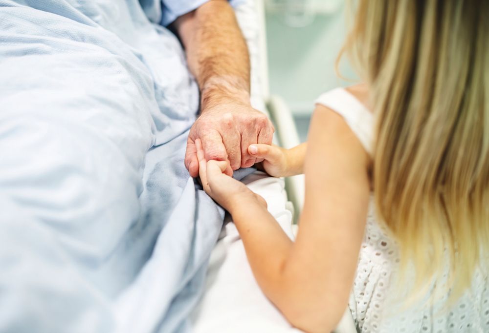 Daughter holding fathers hand in the hospital
