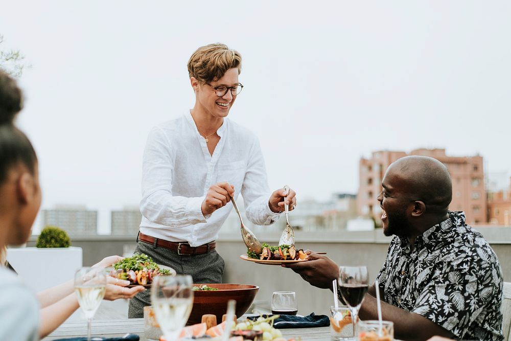 Man serving his friends salad at a rooftop party