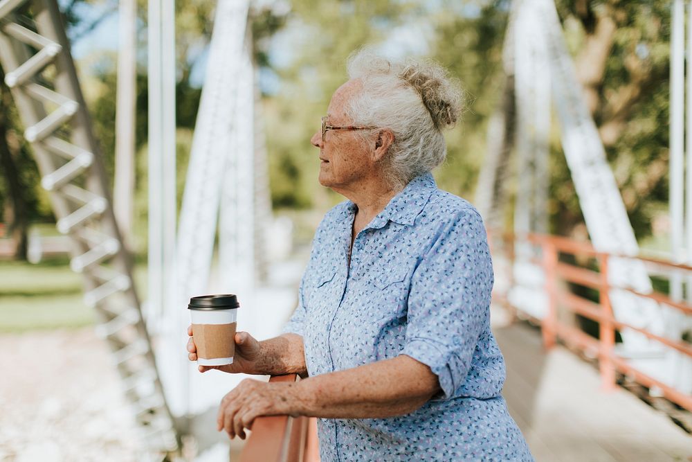 Senior woman standing on a bridge with a coffee