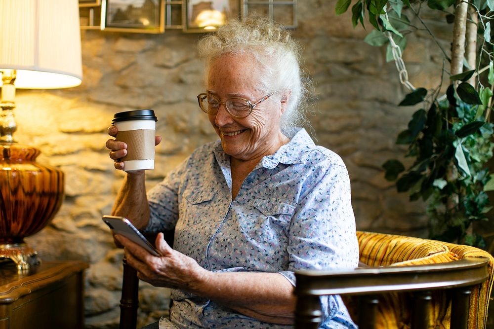 Elderly woman drinking coffee and using her phone