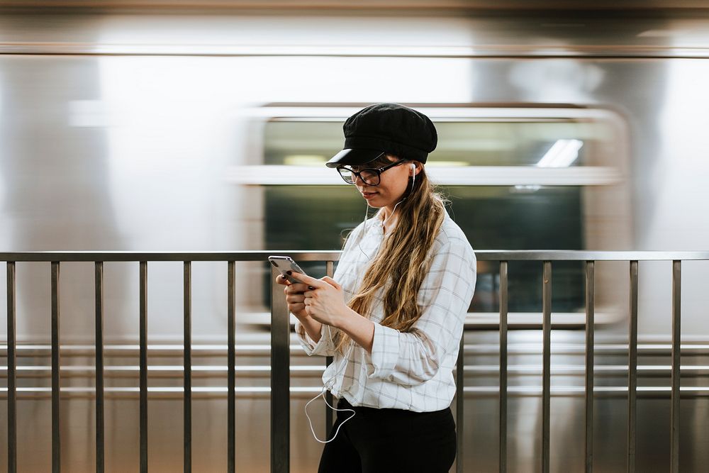 Girl listening to music while waiting for a train at a subway platform