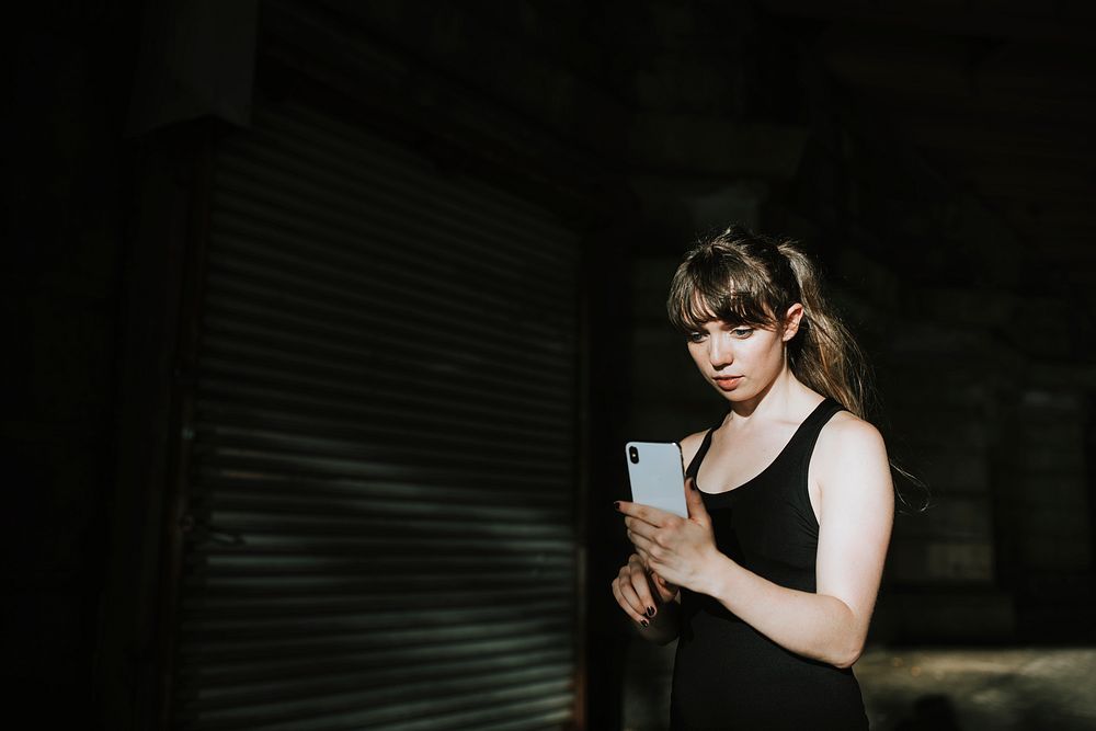 Sporty woman texting in a dark alley