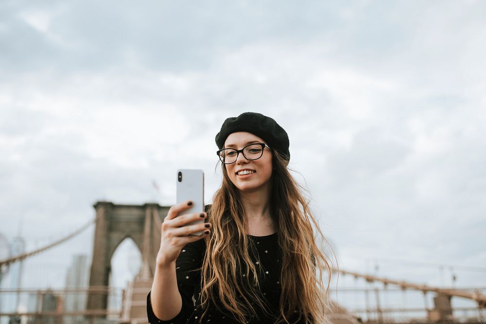 Cheerful woman taking a selfie with The Brooklyn Bridge, USA