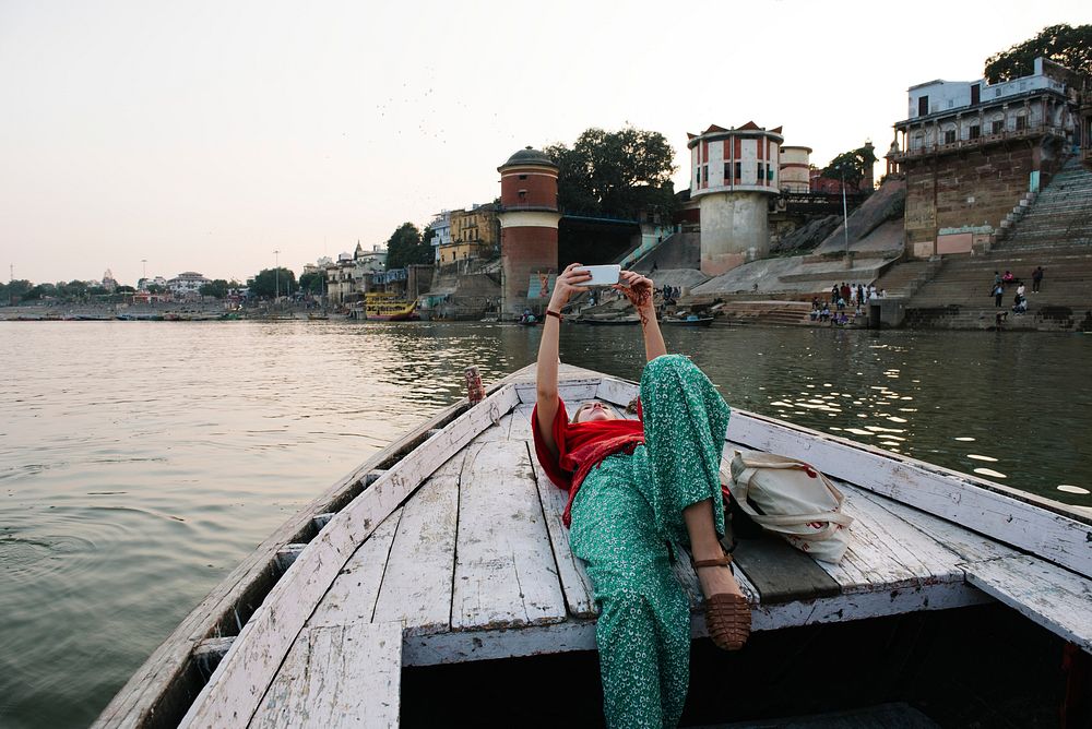Western woman lying on a boat taking selfies in Varanasi