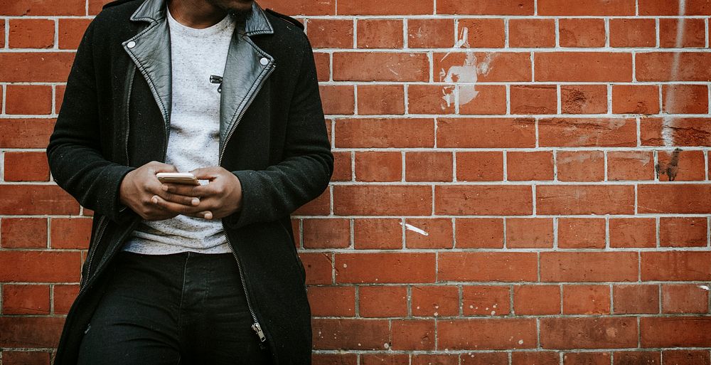 Man texting on his phone by a brick wall