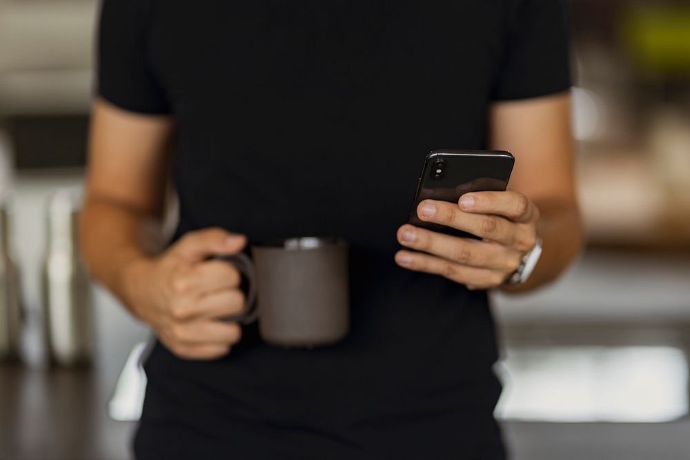 A man texting on his phone while holding a black coffee cup in the other hand