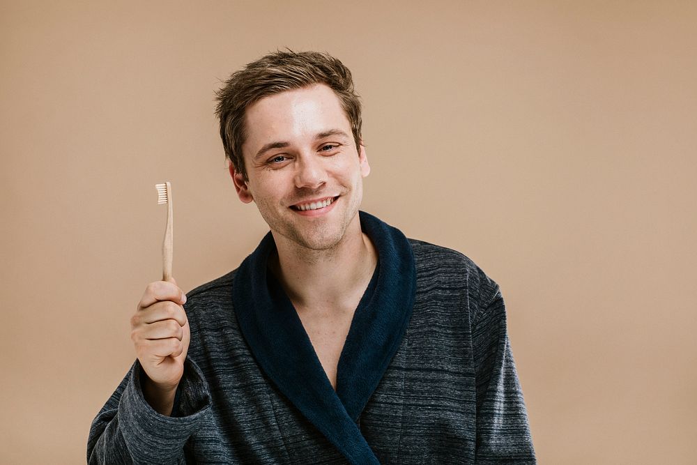 Blond man in a dark robe holding a wooden toothbrush