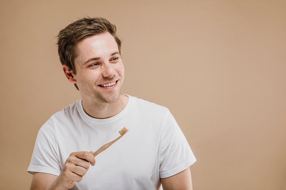 Man in a white tee holding a wooden toothbrush