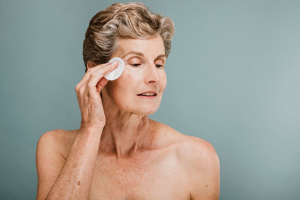 Elderly woman wiping her face with a cotton pad