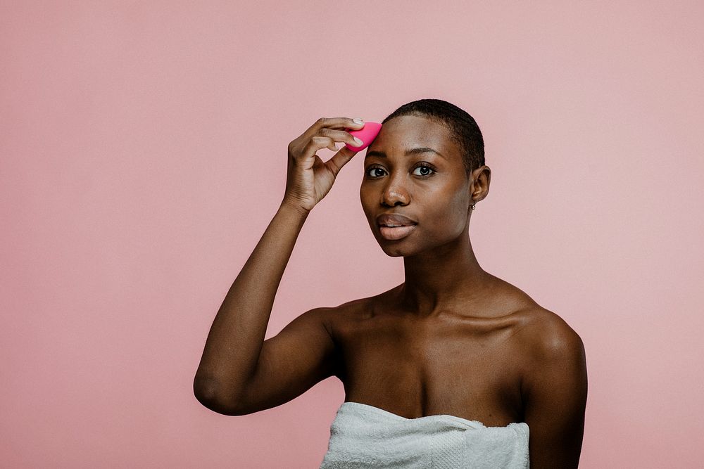 Cheerful black beauty blogger using a pink makeup blending sponge