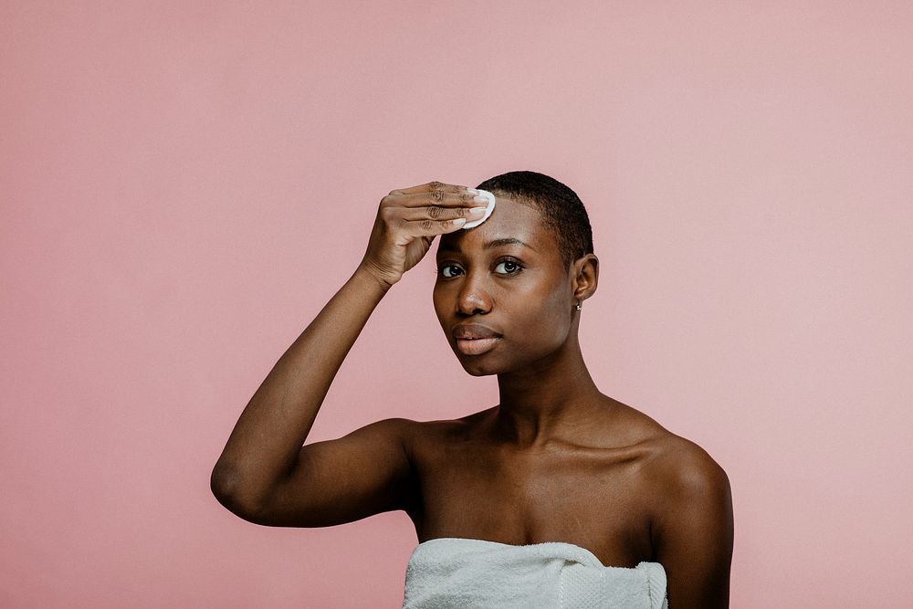 Black woman wiping her face with a cotton pad