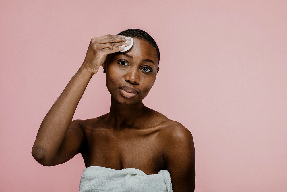 Black woman wiping her face with a cotton pad