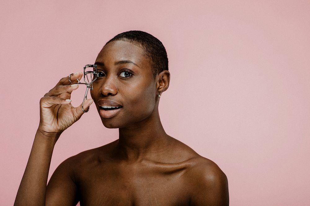 Cheerful black female beauty blogger using an eyelash curler