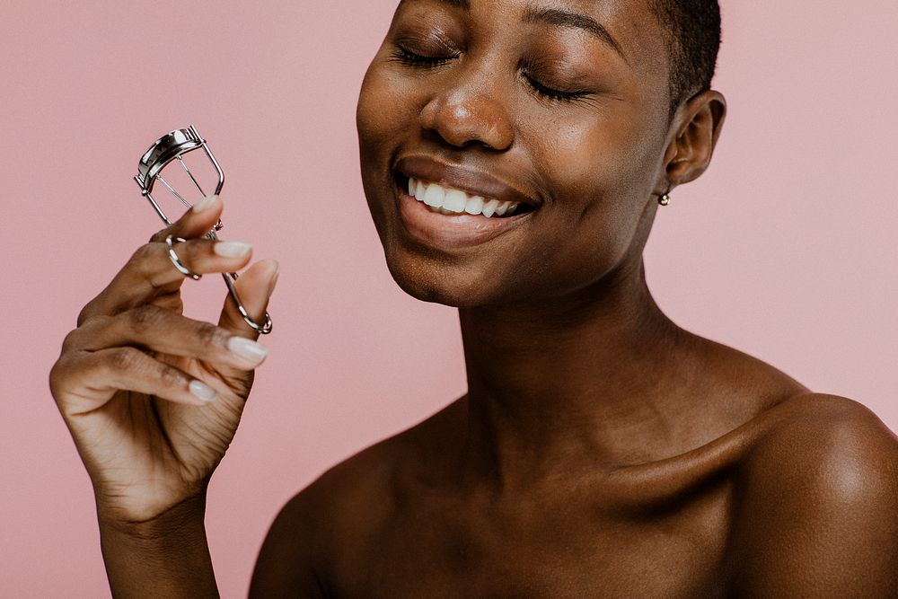 Cheerful black female beauty blogger using an eyelash curler