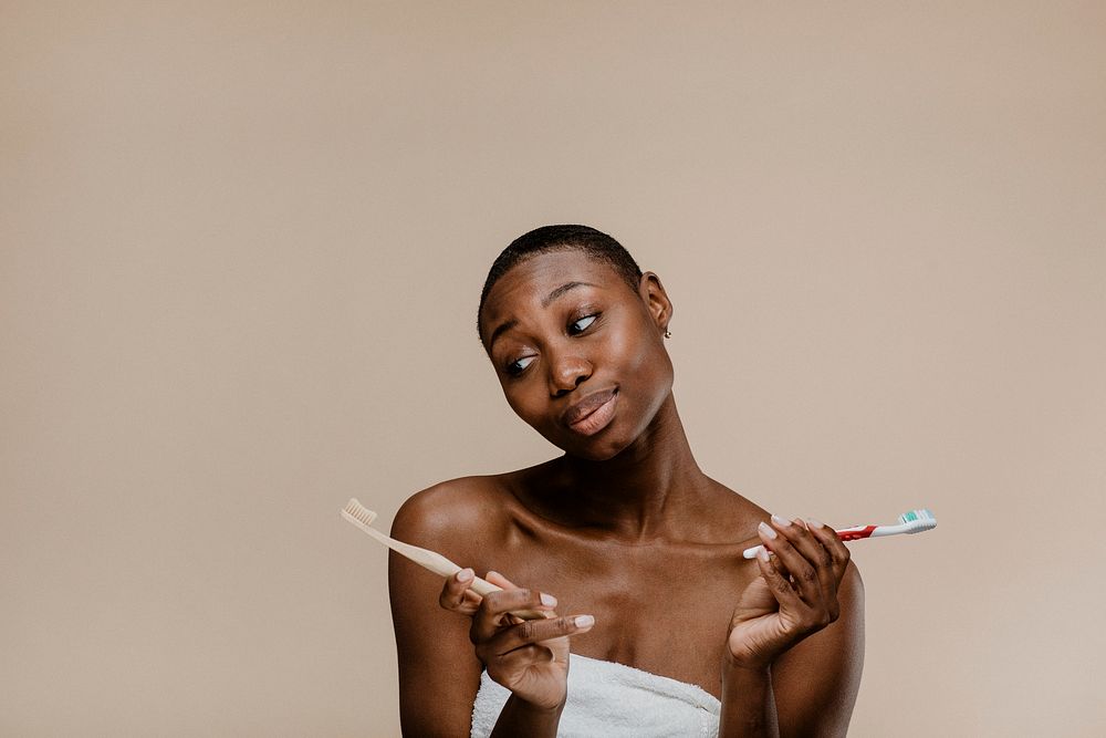Black woman in a towel choosing between a wooden toothbrush and a plastic one