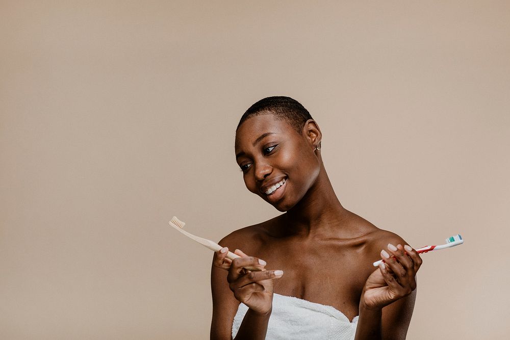 Black woman in a towel choosing between a wooden toothbrush and a plastic one