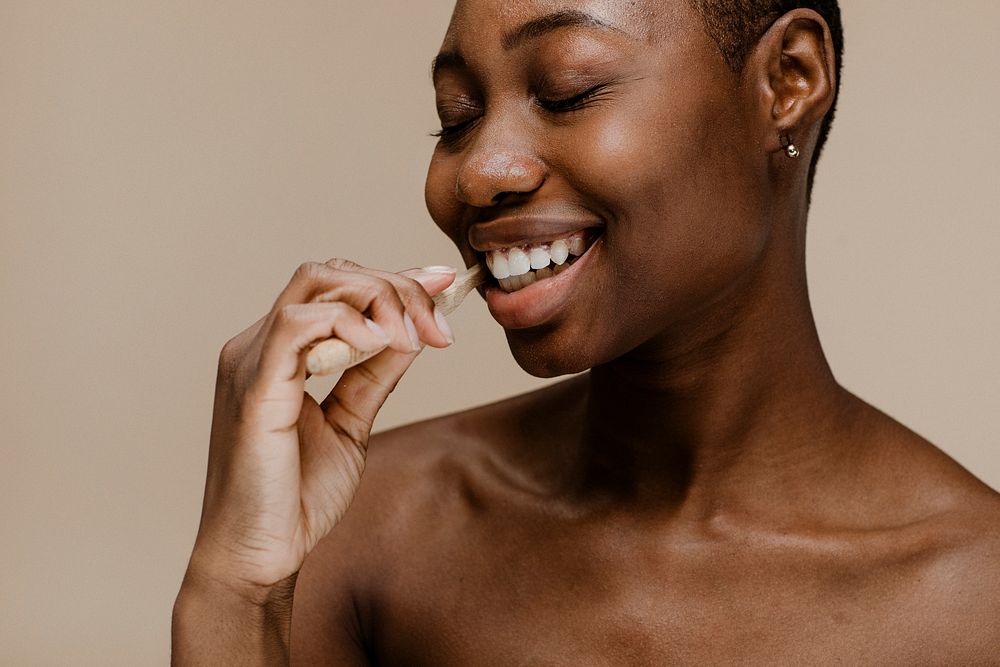 Black woman brushing her teeth with a wooden toothbrush