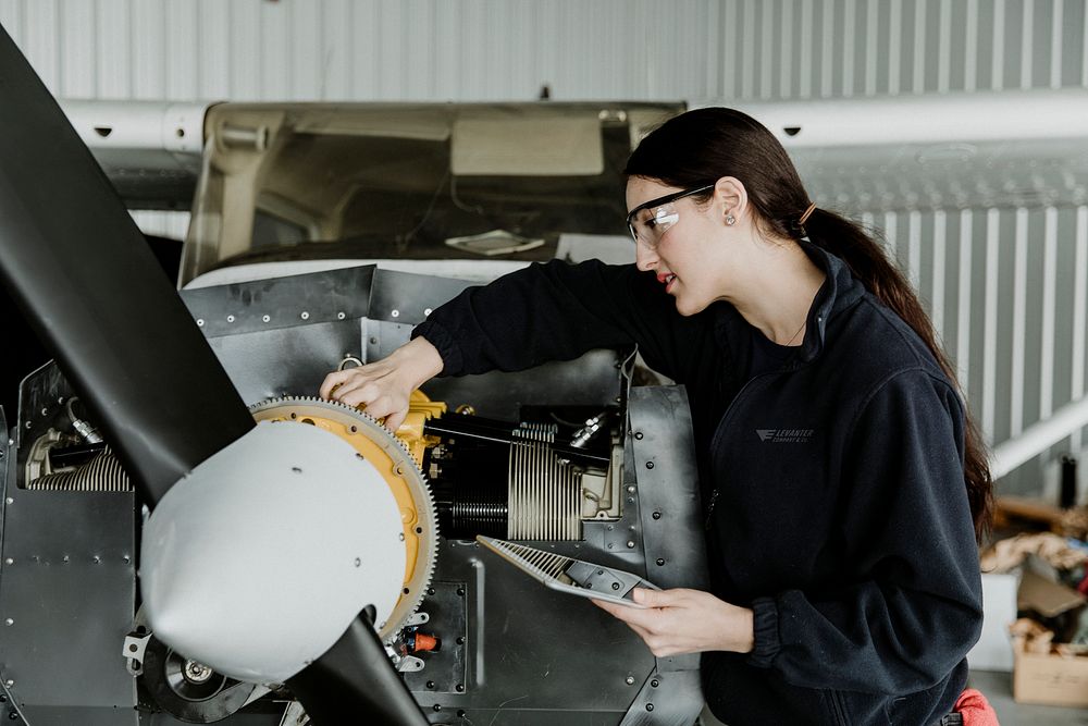 Female aviation technician repairing the motor of a propeller plane