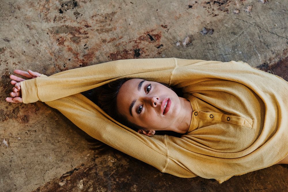 Pierced nose woman in a mustard yellow long sleeve top lying on a concrete floor