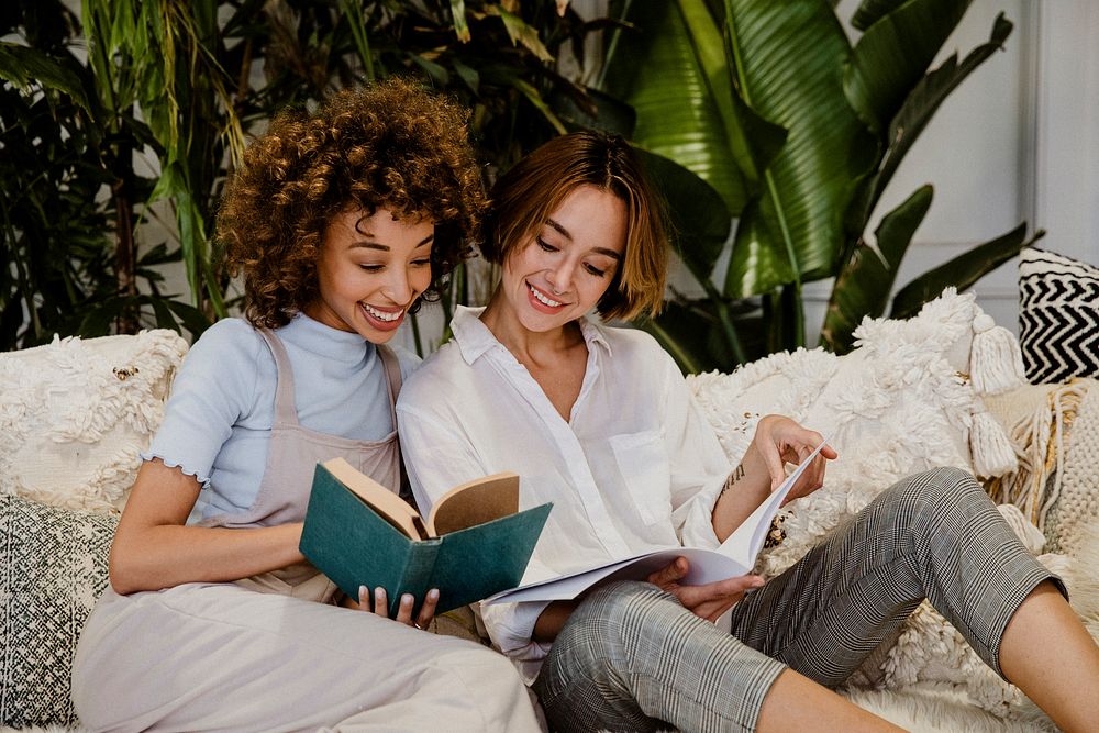 Cheerful lesbian couple reading books on a couch