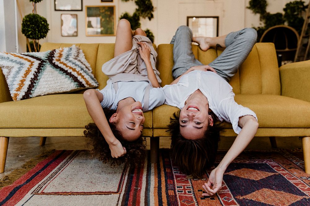 Cheerful women lying upside down on a mustard yellow couch