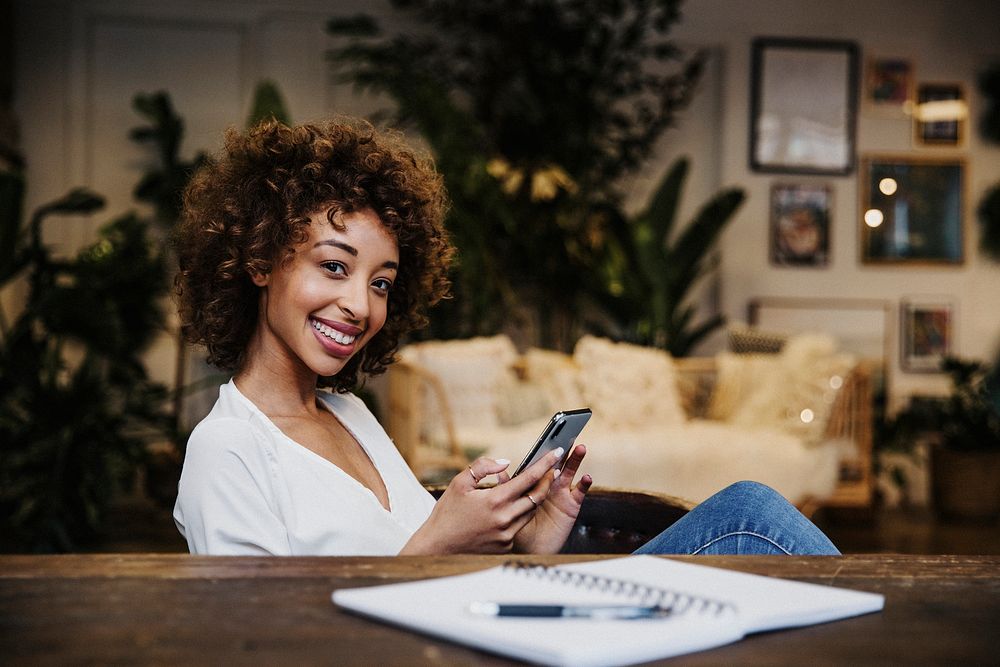 Cheerful black woman using her phone at her wooden table