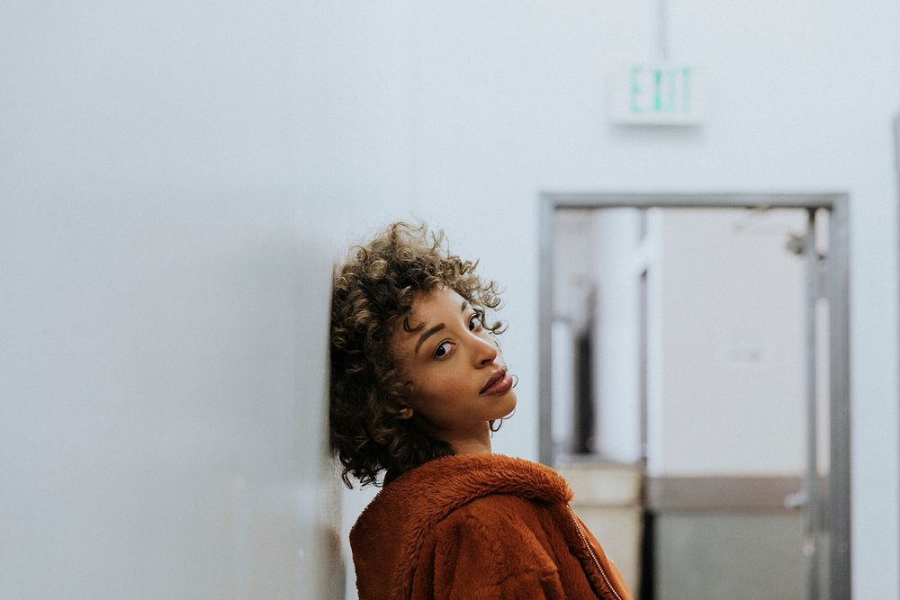 Woman in a brown coat leaning against a wall