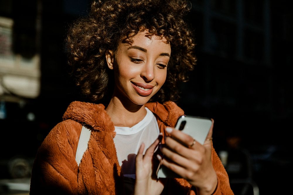 Cheerful black woman using her phone in downtown