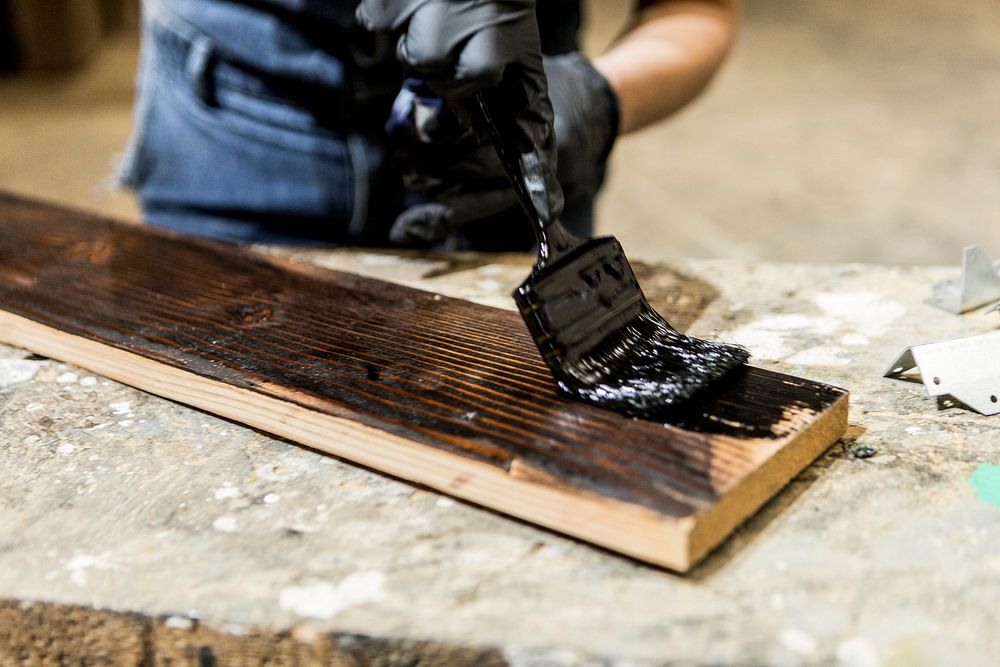 Female carpenter coating lumber with lacquer