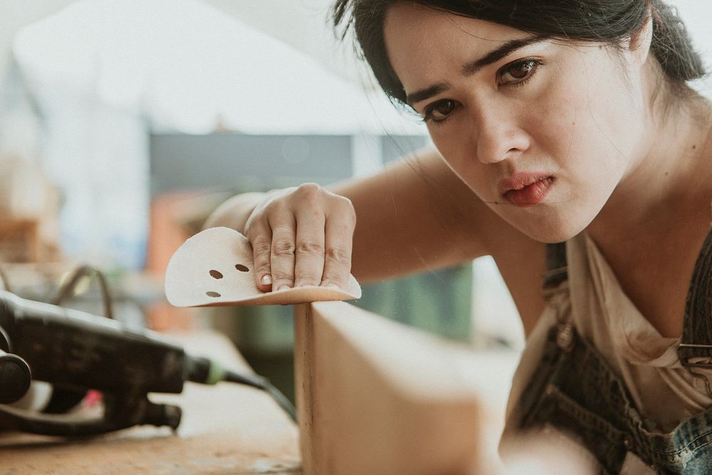 Female carpenter smoothing the lumber with a sanding disc