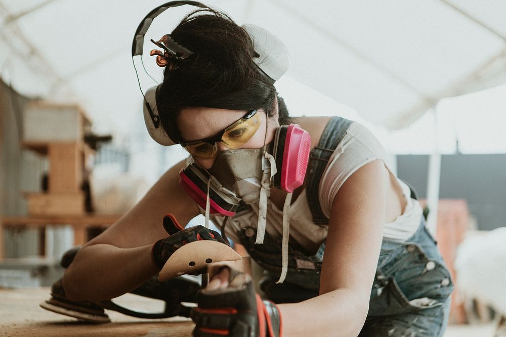 Female carpenter smoothing the lumber with a sanding disc