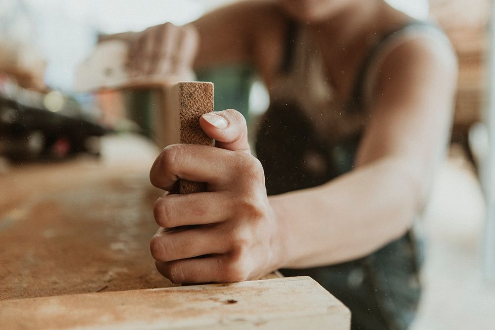 Female carpenter smoothing the lumber with a sanding disc