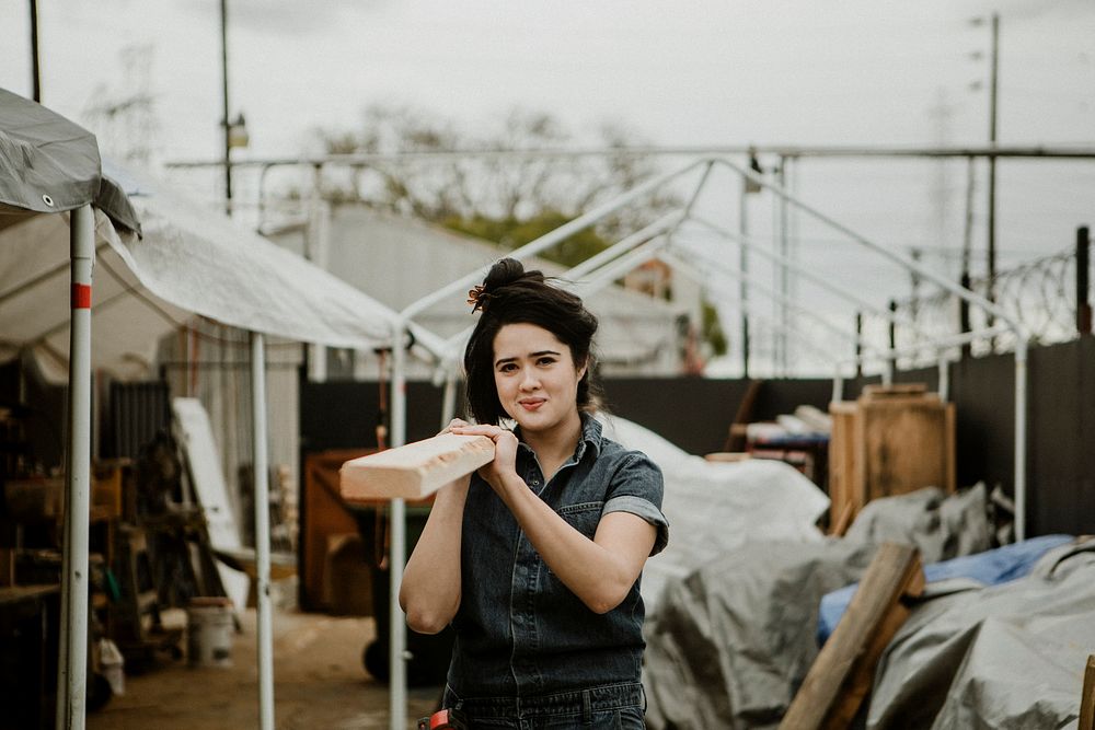 Female carpenter carrying a lumber on her shoulder