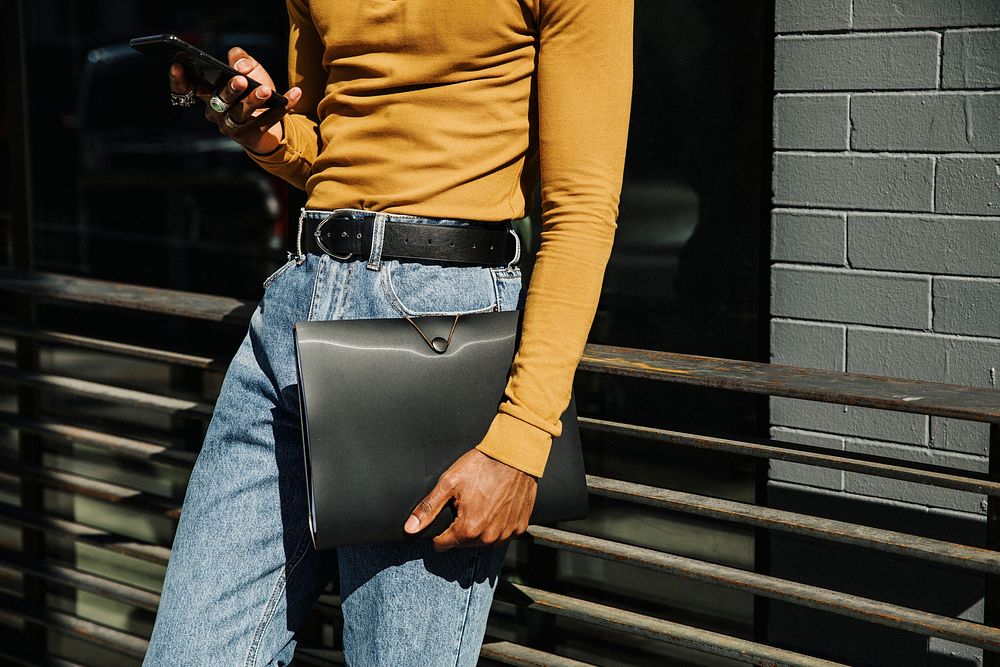 Man in a mustard yellow long sleeve top with a black folder briefcase using a phone