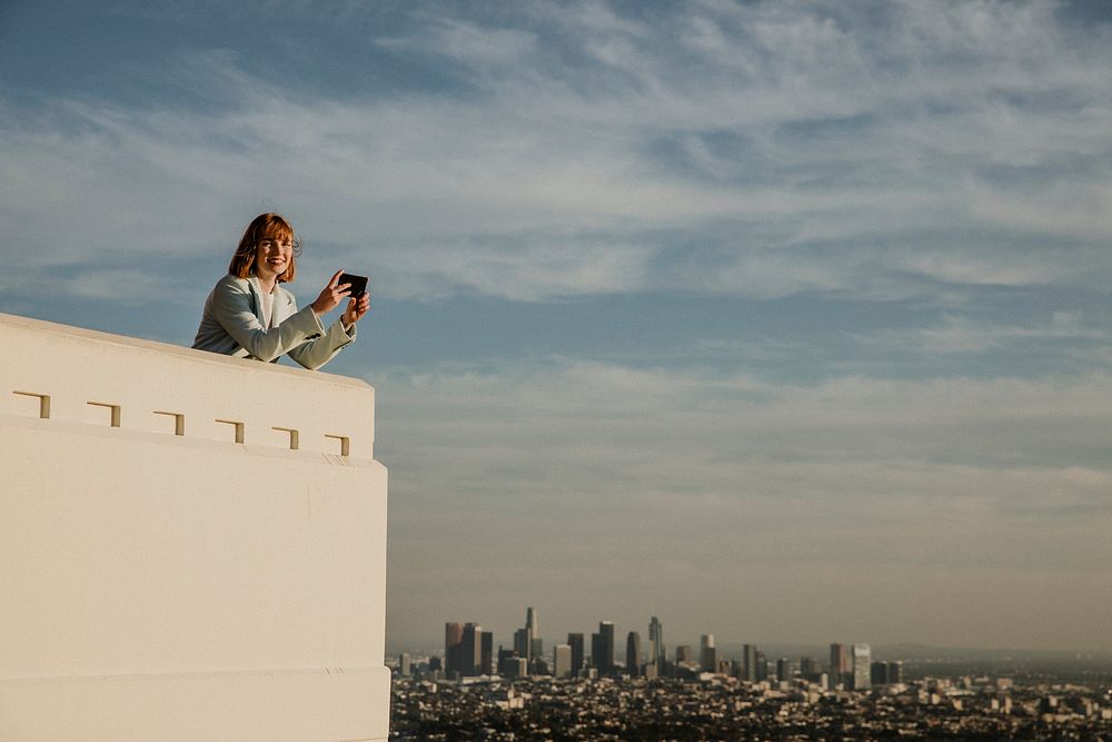 Woman capturing the Los Angeles view with her phone at the Griffith Observatory, USA