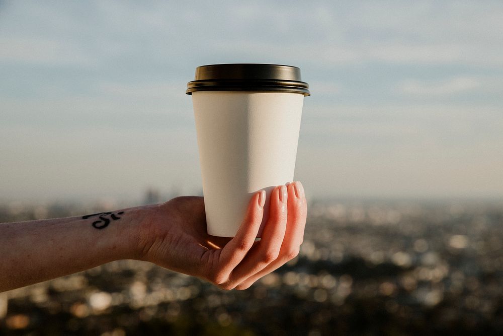 Hand holding a takeout coffee cup with urban view mockup