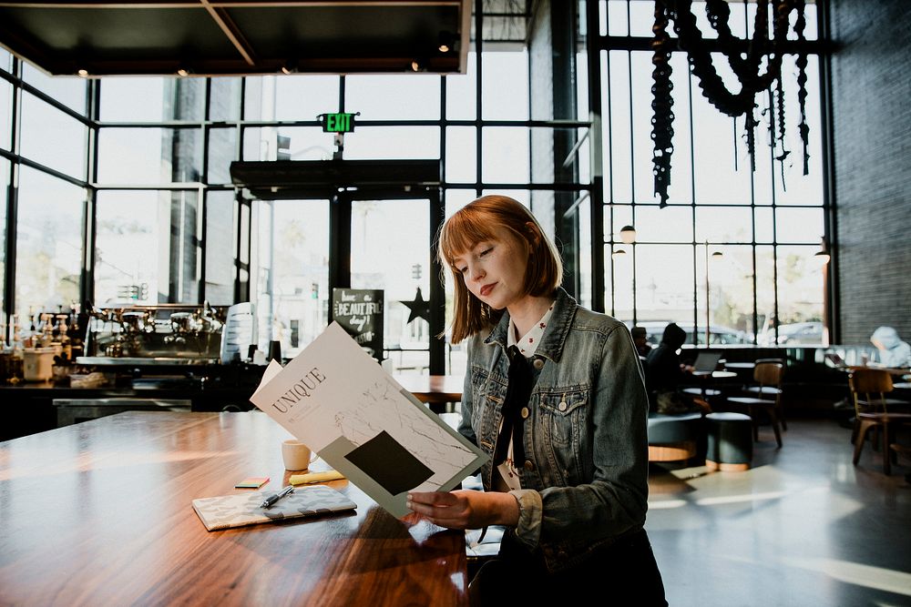 Cheerful woman reading a magazine in a cafe