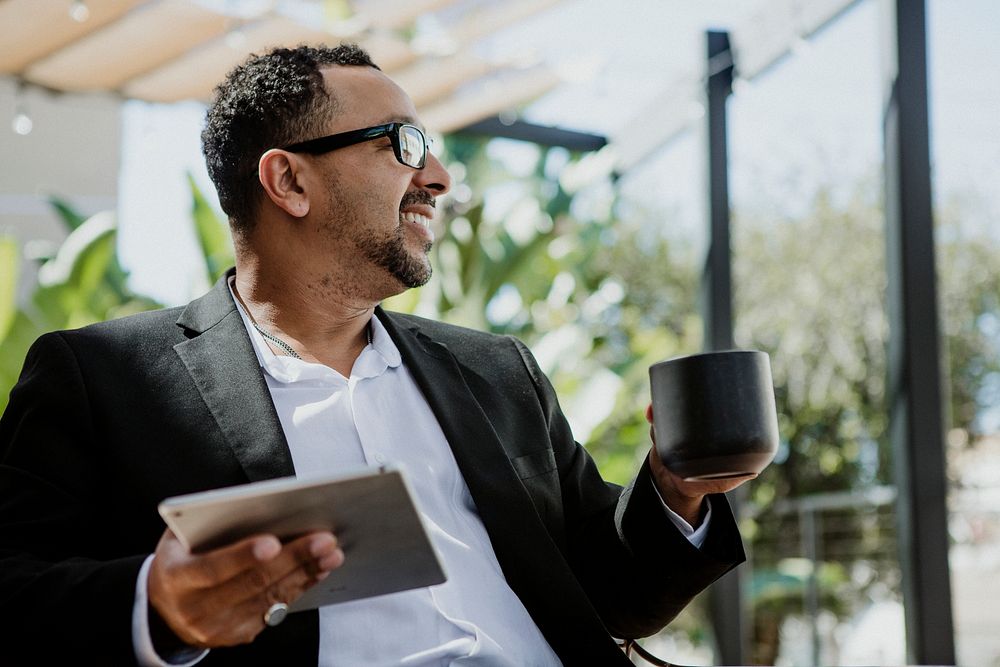 Happy businessman enjoying a coffee while using a tablet
