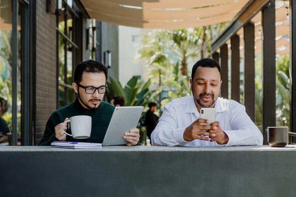 Men working with digital devices in a cafe