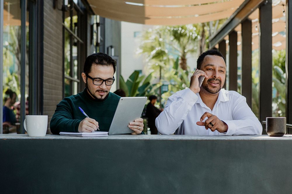 Men working with digital devices in a cafe