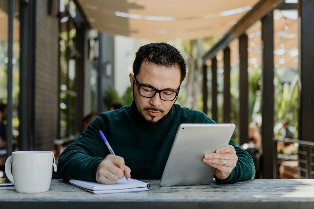 Man making notes while using a tablet