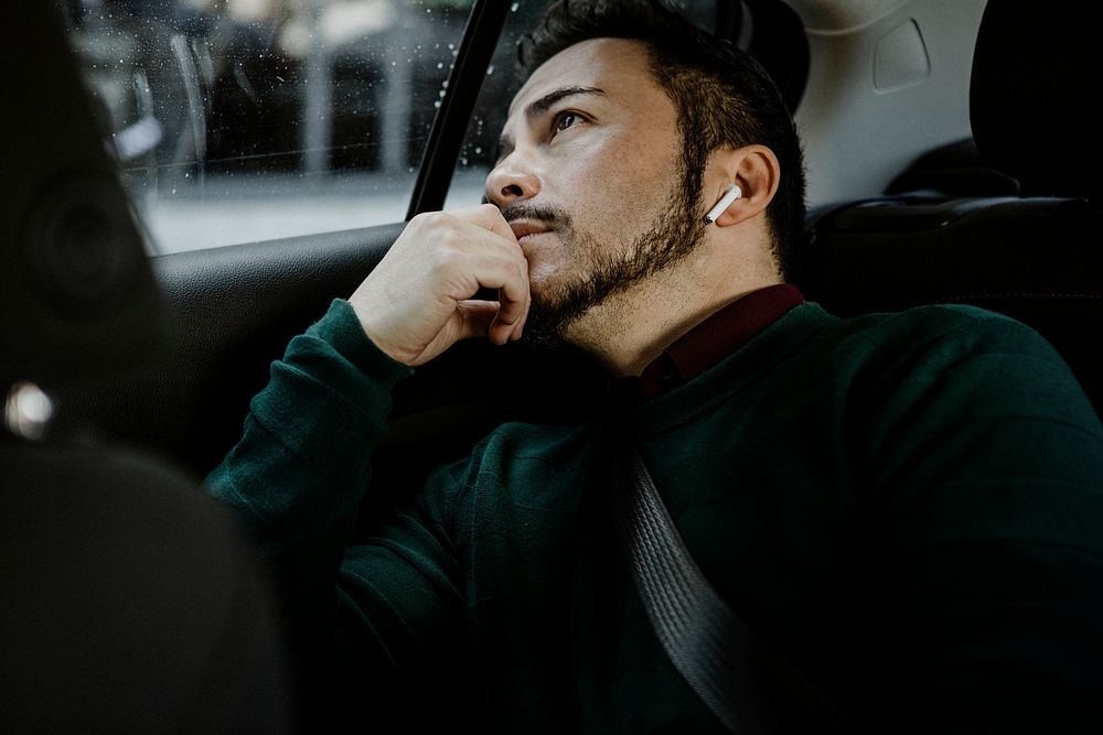 Man in a car with wireless earphones looking out the window