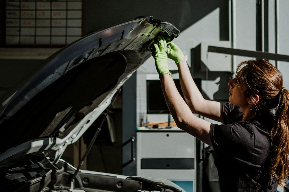 Female mechanic opening a car hood