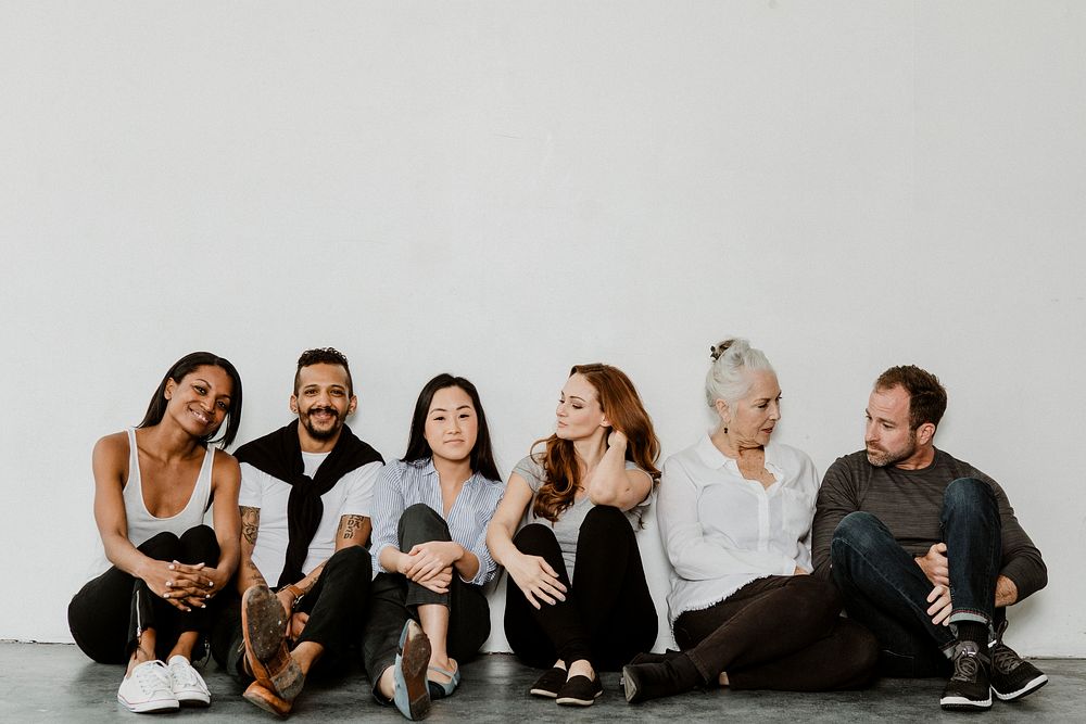 Group of cheerful diverse people sitting on a floor in a white room