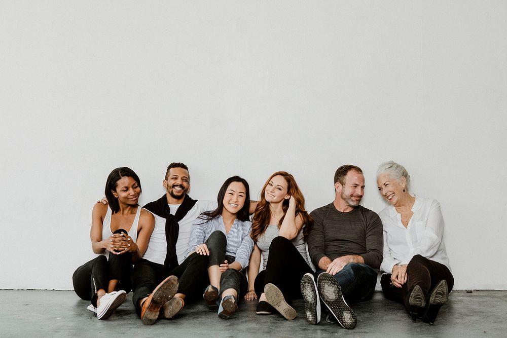 Group of cheerful diverse people sitting on a floor in a white room