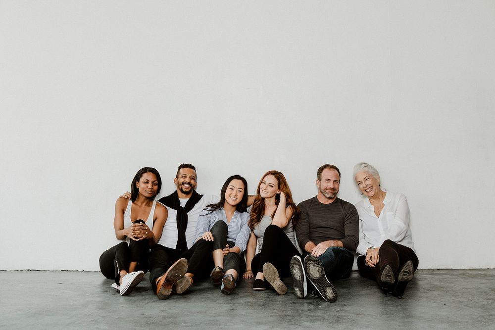 Group of cheerful diverse people sitting on a floor in a white room