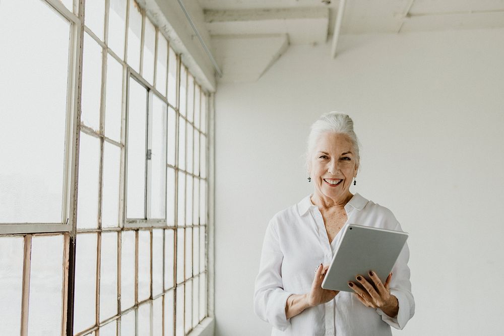 Senior woman using a digital tablet by the window in a white room